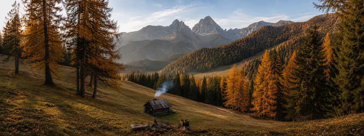 Larici in autunno e una baita con il camino acceso, sotto le cime dolomitiche